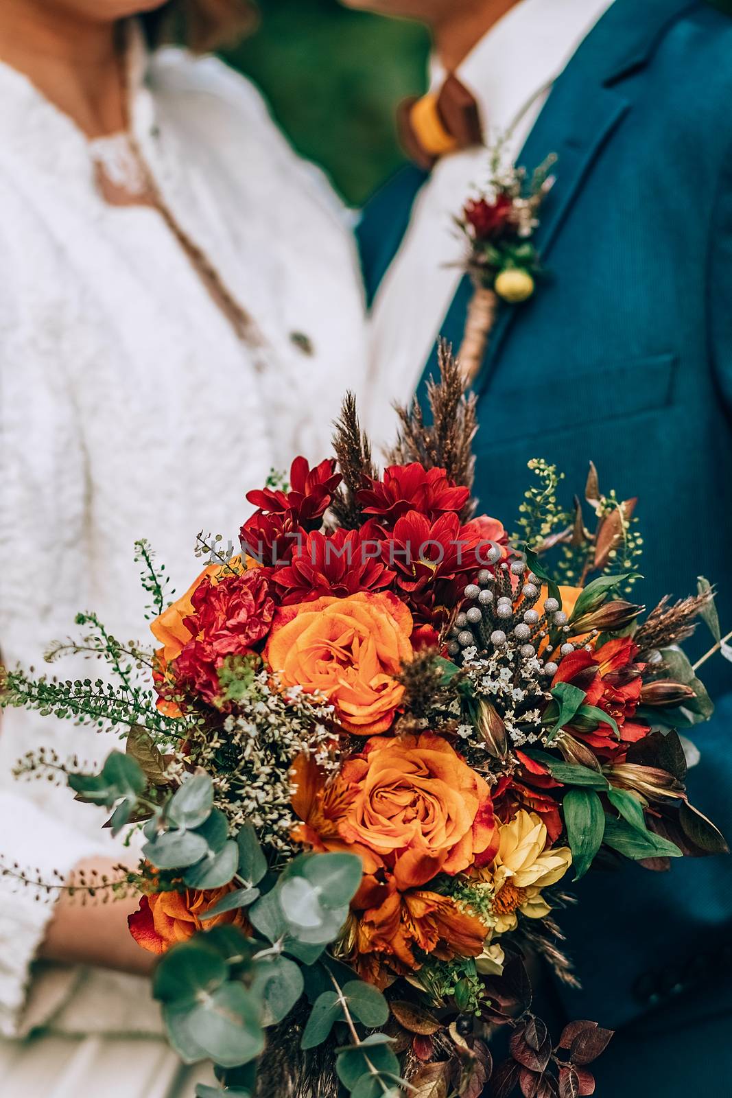 Crop blurred just married couple in elegant clothes hugging and holding beautiful bouquet of fresh colorful flowers in composition with green and brown herbs