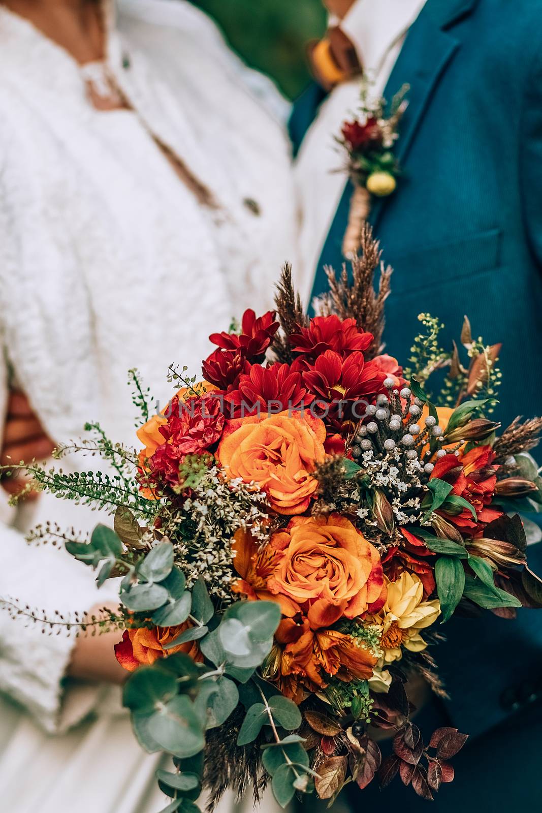 Crop blurred just married couple in elegant clothes hugging and holding beautiful bouquet of fresh colorful flowers in composition with green and brown herbs