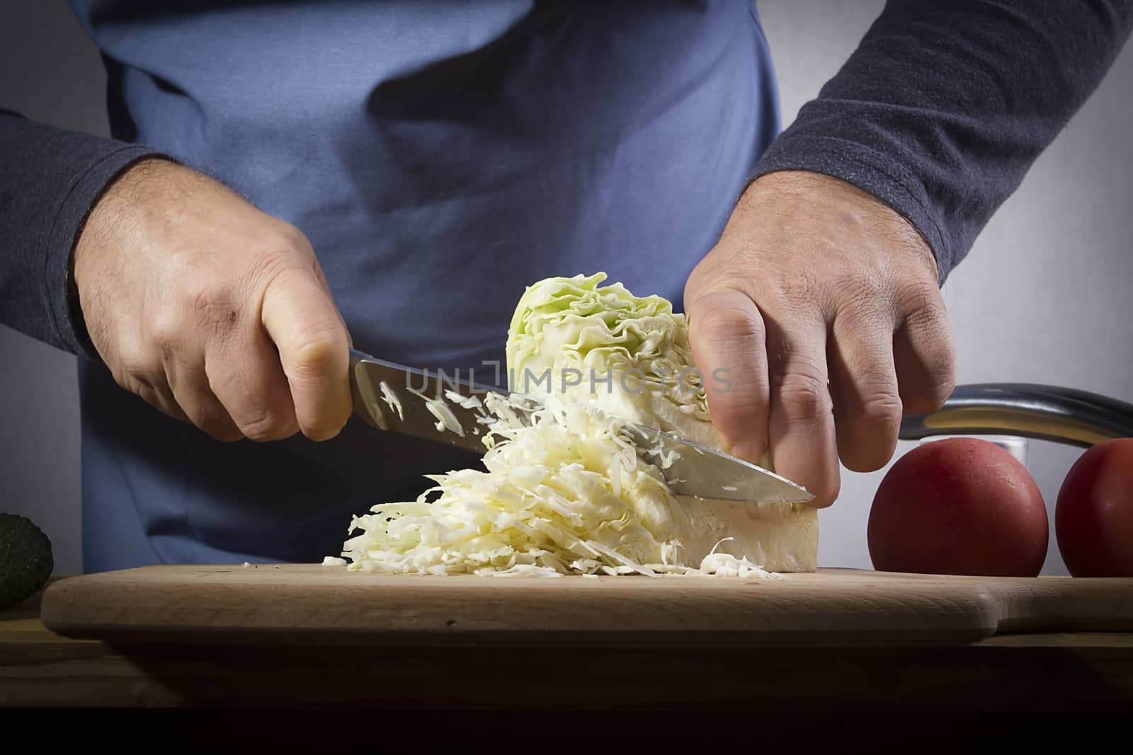 Hands with a knife chopping cabbage on the kitchen table