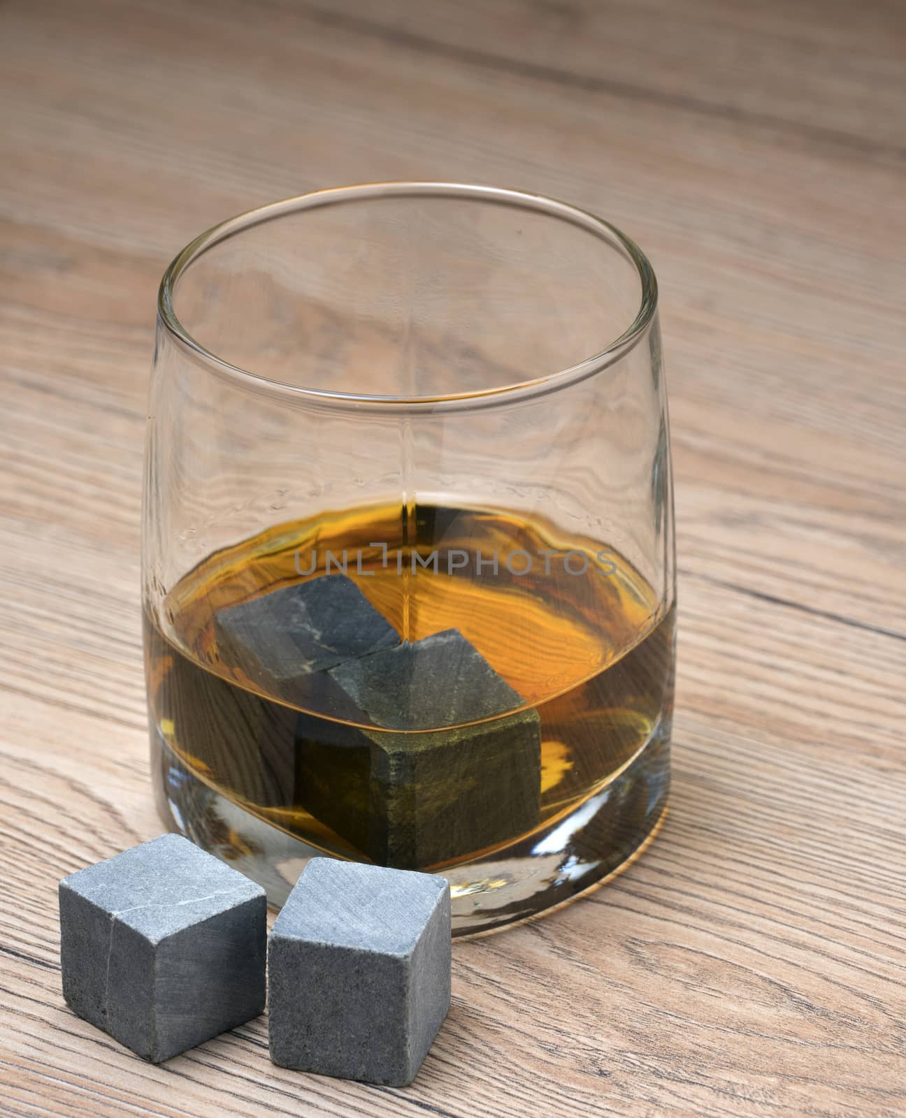 Glass with whiskey and whiskey stones on wooden background
