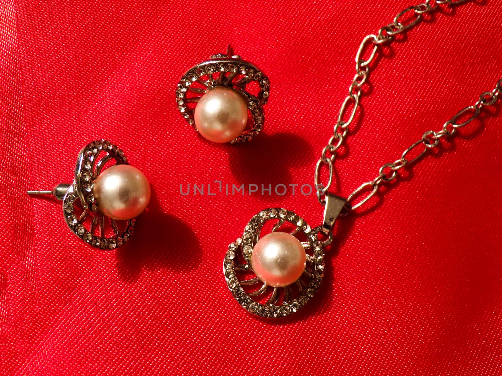 Beautiful earrings and pendant on a chain. Set of jewelry made of silver on a silk red fabric close up. Jewelry made of precious metals and stones.