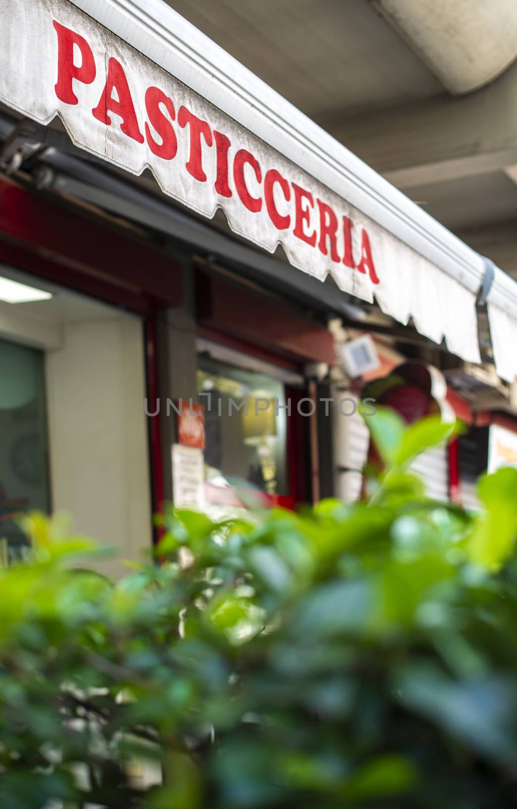 Text pasticceria on sunblind. Italian pastry shop. Facade on pastry shop.  Green foliage in front of cafe and sweets shop.