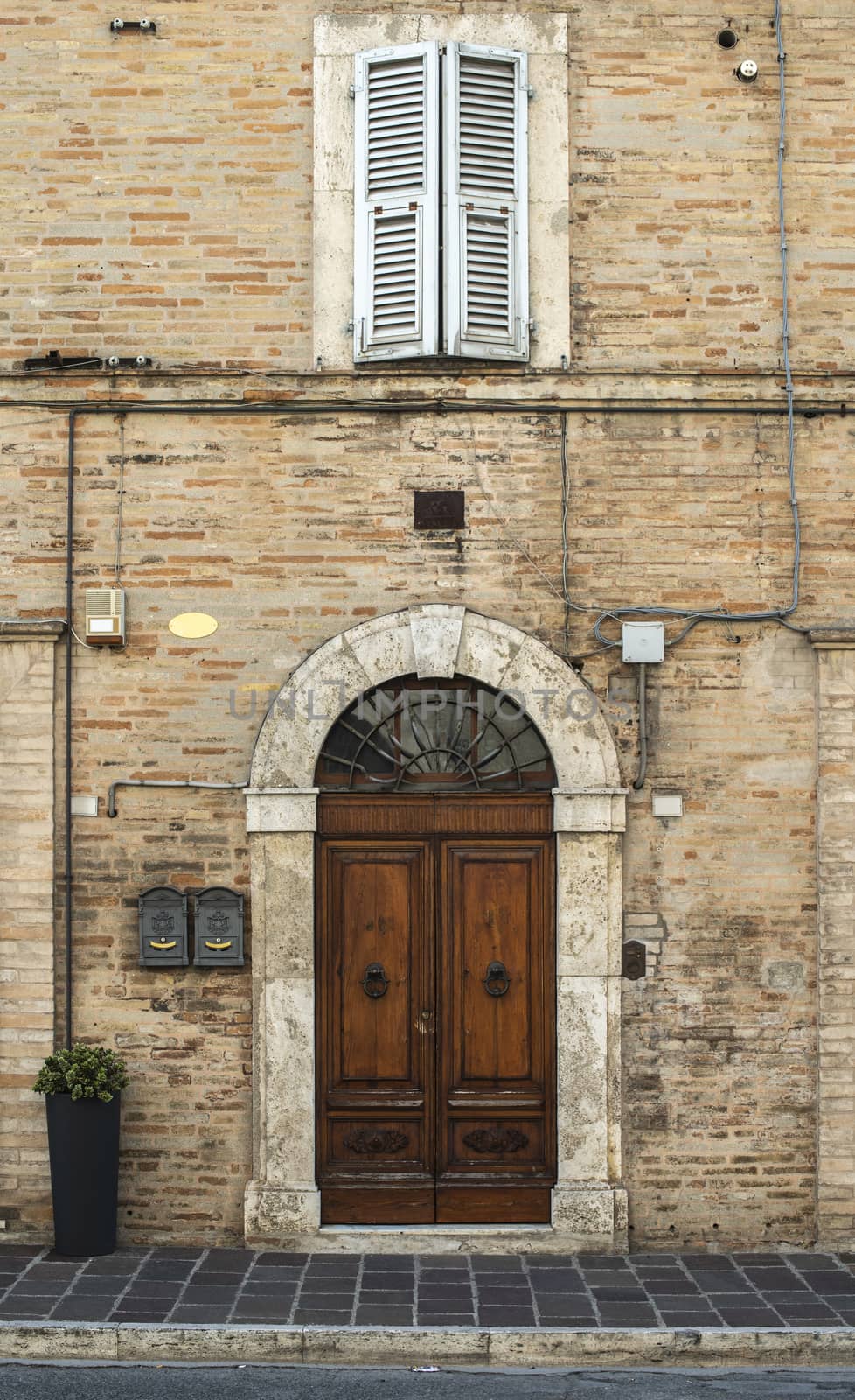 Old typical italian wooden door. Italian house. Ancient house facade. Sunlight. Round door arch. Stone build house. Wrought iron door handles.