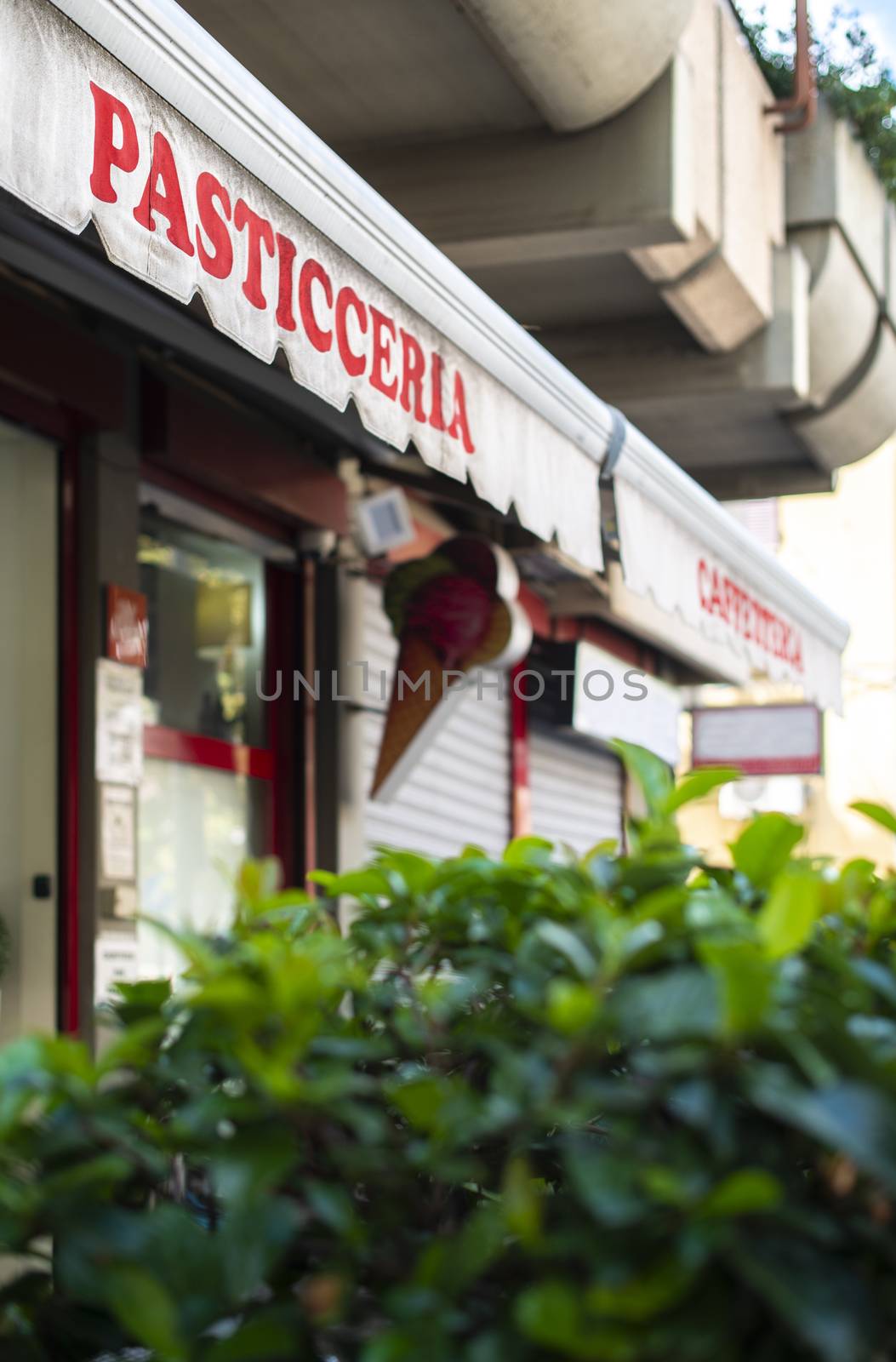 Text pasticceria on sunblind. Italian pastry shop. Facade on pastry shop.  Green foliage in front of cafe and sweets shop.