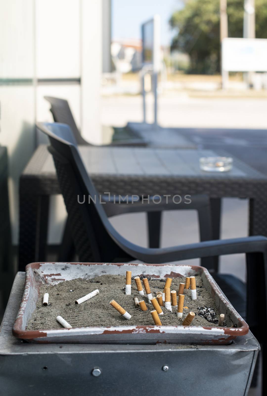 Ashtray with sand and buried cigarettes. Table and chairs. Many cigarette butts.