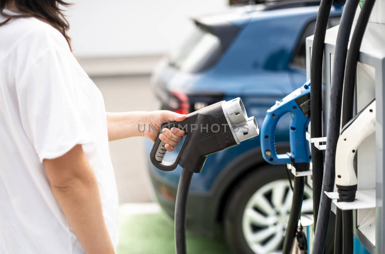 Woman charge her Electric car on gas station. Blue car and electric plug for charging. Ecology fuell concept.