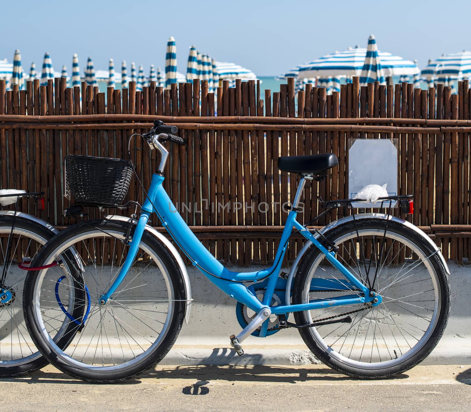 Rental bikes on the beach. Blue bicycles on the street. Many beach umbrellas.