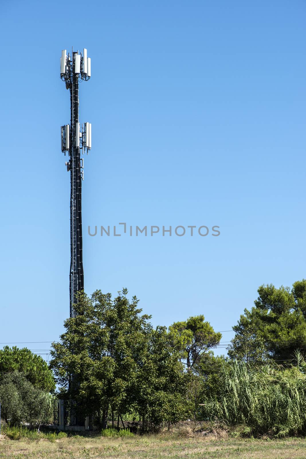 Telecommunication 5G transmitters. GSM antenna on blue sky. Antenna in the nature. New 5G technology concept. Green foliage and trees.