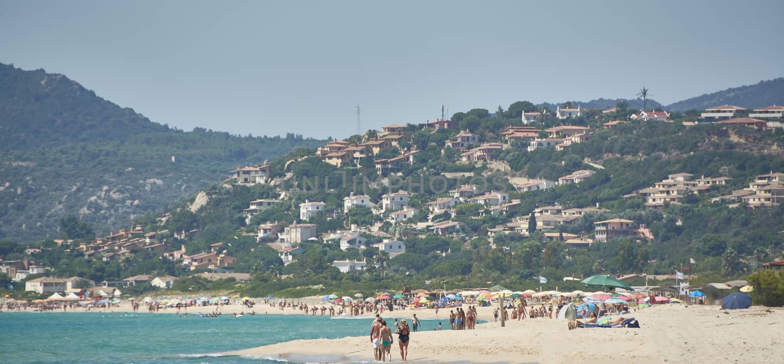Image of the town of Costa Rei in Sardinia taken from the crowded beach during the daytime.