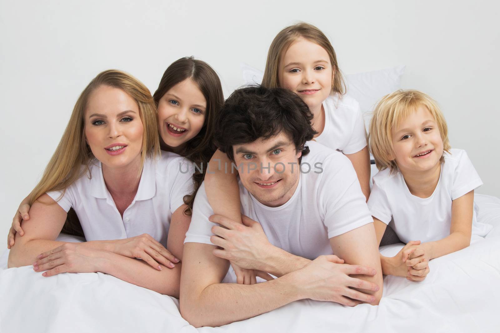 Family of parents and three children in white clothes laying on white background