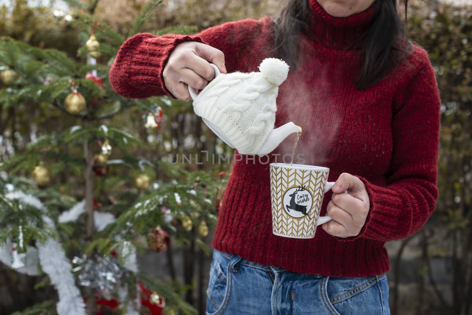 Woman pours tea with a teapot into a teacup. Christmas tree in t by deyan_georgiev