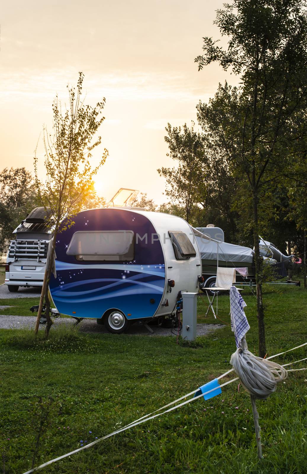 Caravans and campers on green meadow in campsite. Sunrise, rays on campers in the morning. Green grass. Outdoor concept for traveling and res in the nature.
