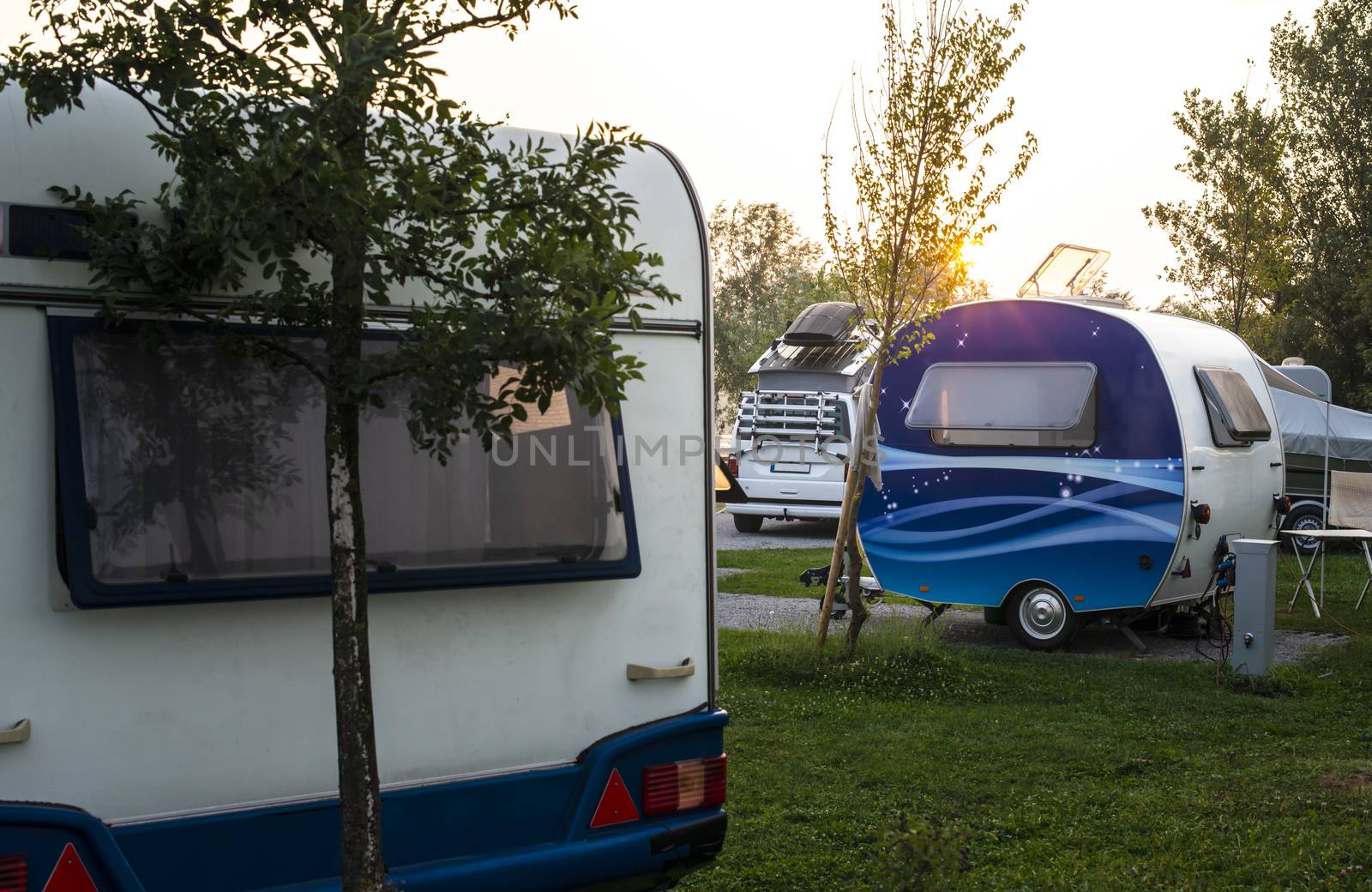 Caravans and campers on green meadow in campsite. Sunrise, rays on campers in the morning. Green grass. Outdoor concept for traveling and res in the nature.