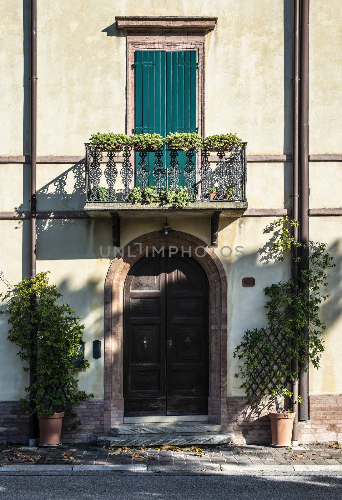 Italian style house facade. Door and terrace with flowers. Sunlight on the wall.