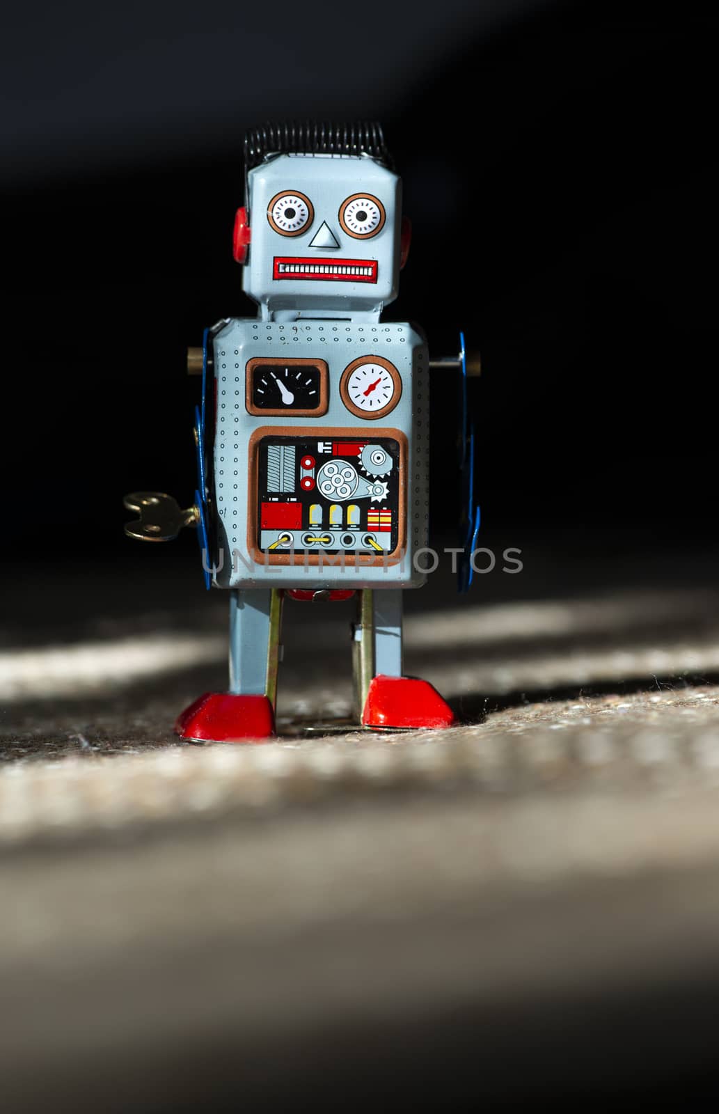 Vintage metal blue robot toy on sunlight. Futuristic concept with small mechanical robot toy walking on cloth surface. Painted eyes and electronic dashboard. Mechanical toy key. Hard light and shadows.