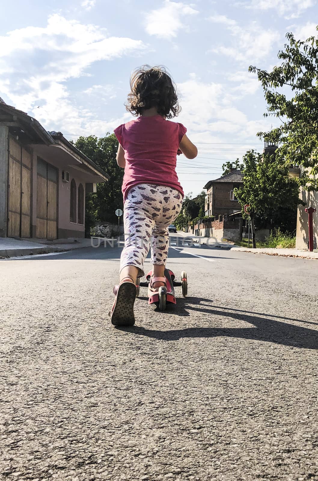 Little girl play with scooter on the street. by deyan_georgiev
