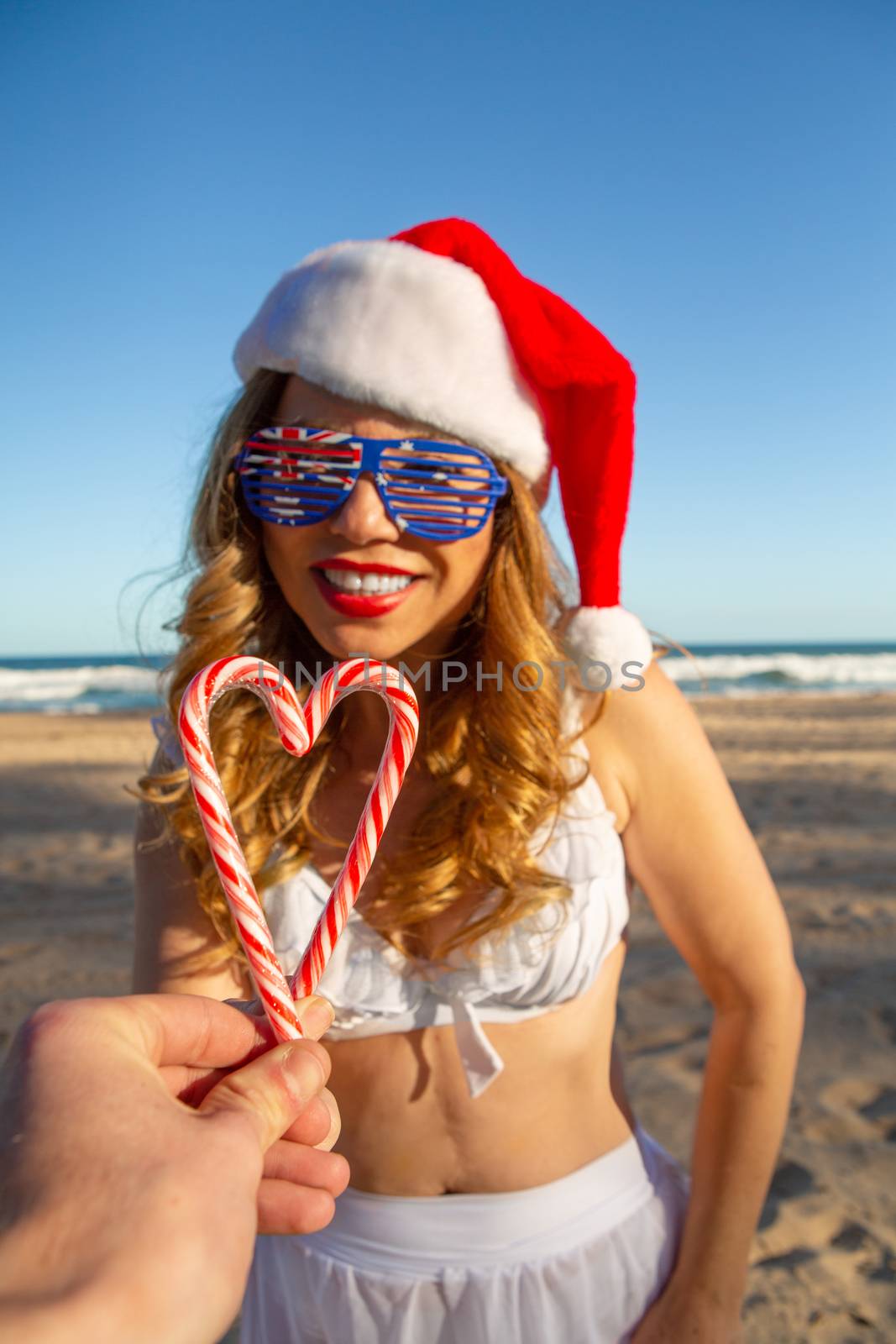 Two friends  join their candy canes together to form a heart, at the beach at Christmas time, a fun symbol of friendship, bondship, mates, love,  festive season.  Selective focus to candy canes only