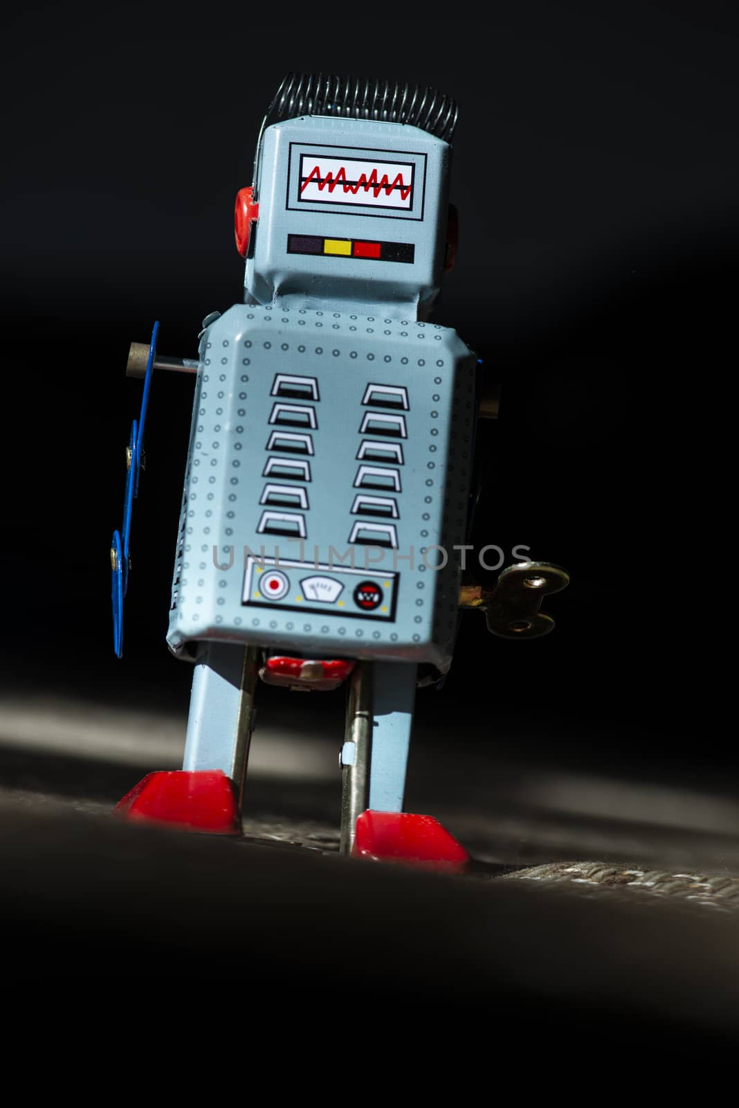 Vintage metal blue robot toy on sunlight. Futuristic concept with small mechanical robot toy walking on cloth surface. Painted eyes and electronic dashboard. Mechanical toy key. Hard light and shadows.