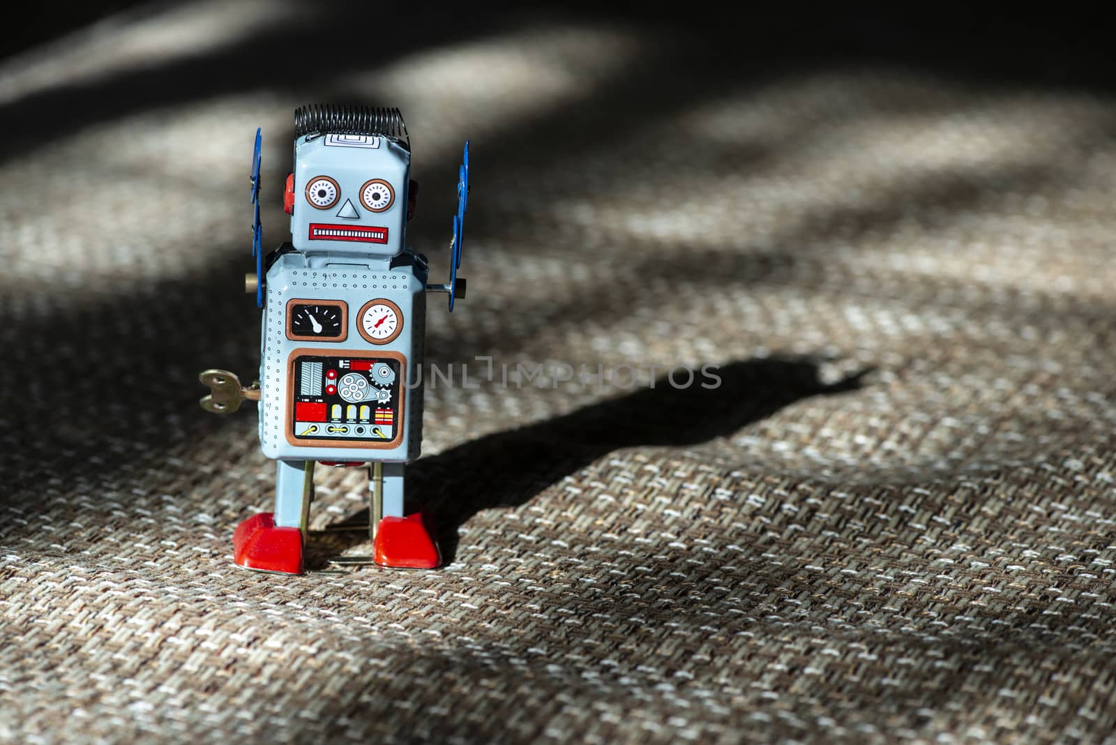 Vintage metal blue robot toy on sunlight. Futuristic concept with small mechanical robot toy walking on cloth surface. Painted eyes and electronic dashboard. Mechanical toy key. Hard light and shadows.