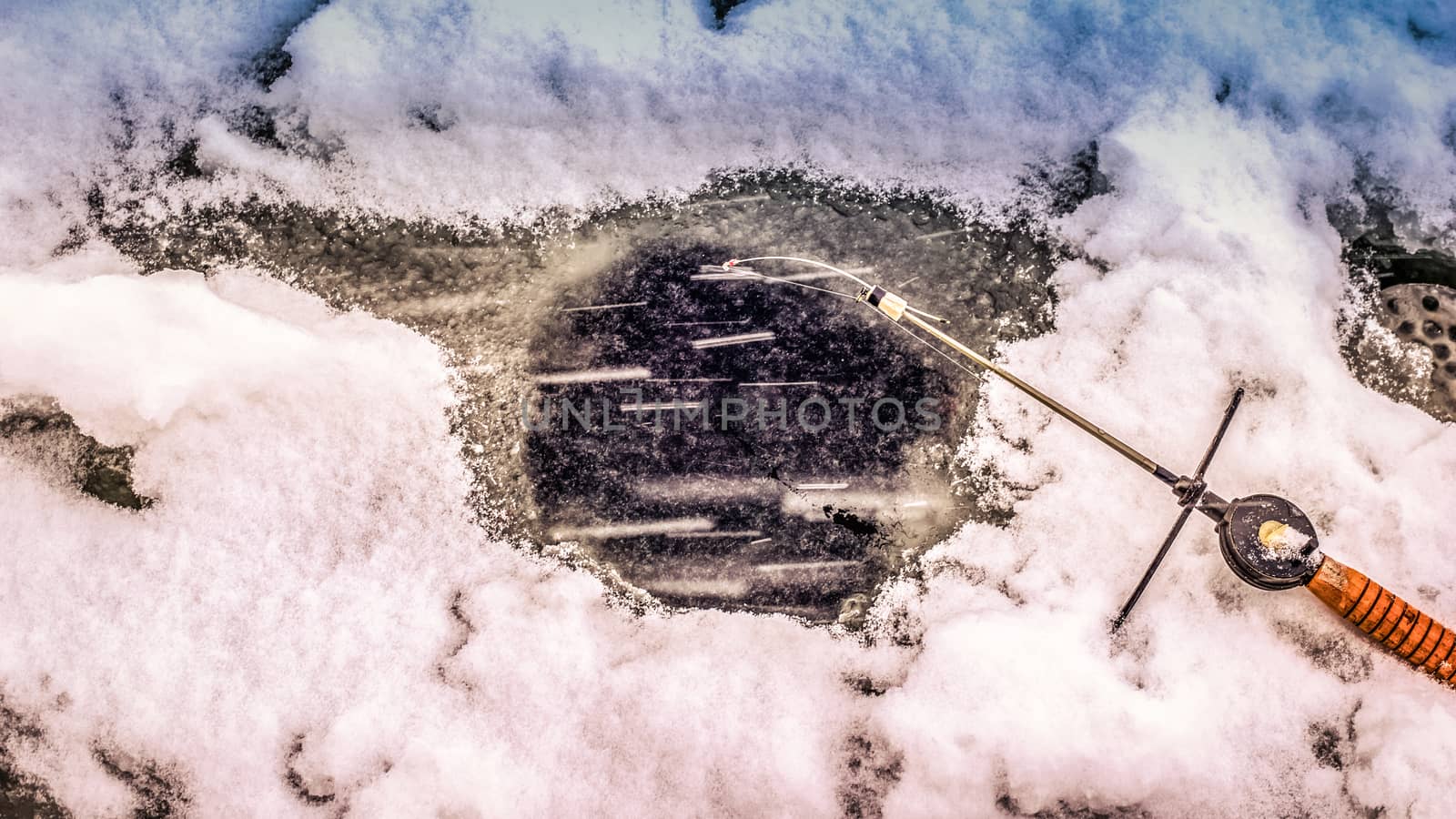 A fishing rod lies near the hole in the ice on the river in winter. Winter fishing