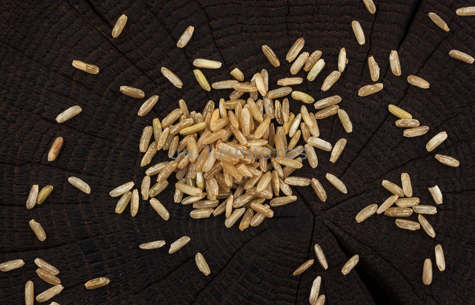 Heap of brown rice groats on black wooden background, top view