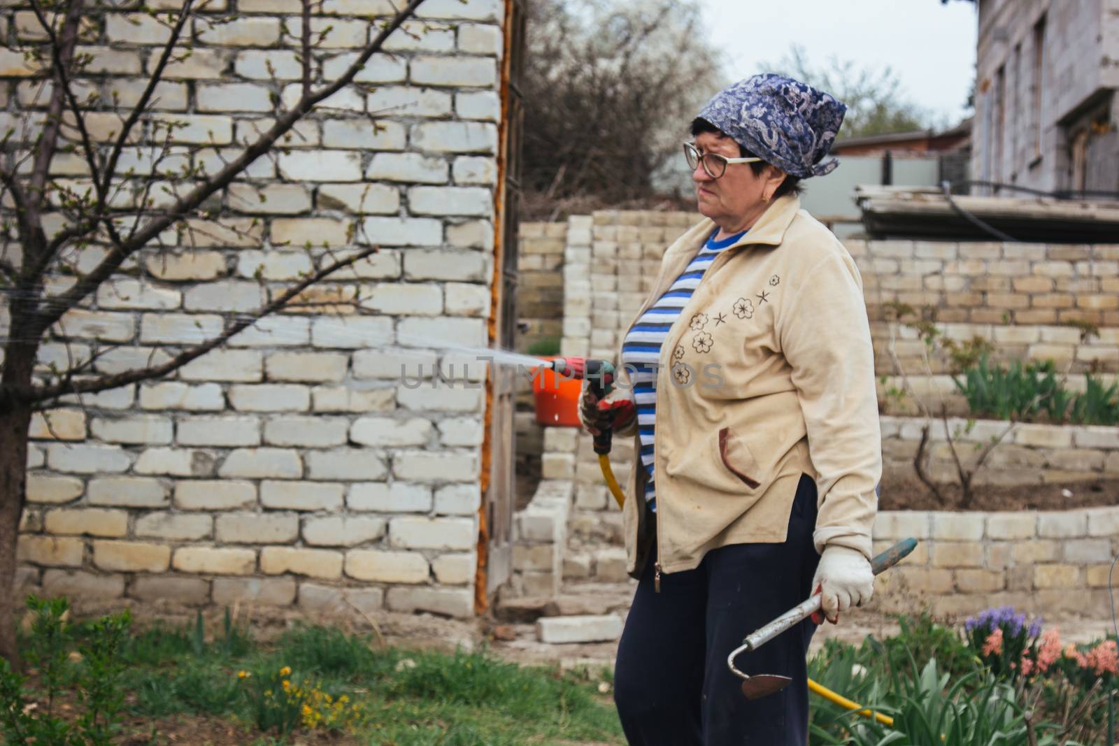 Woman holding garden water hose wearing colorful wellies watering garden by yulaphotographer