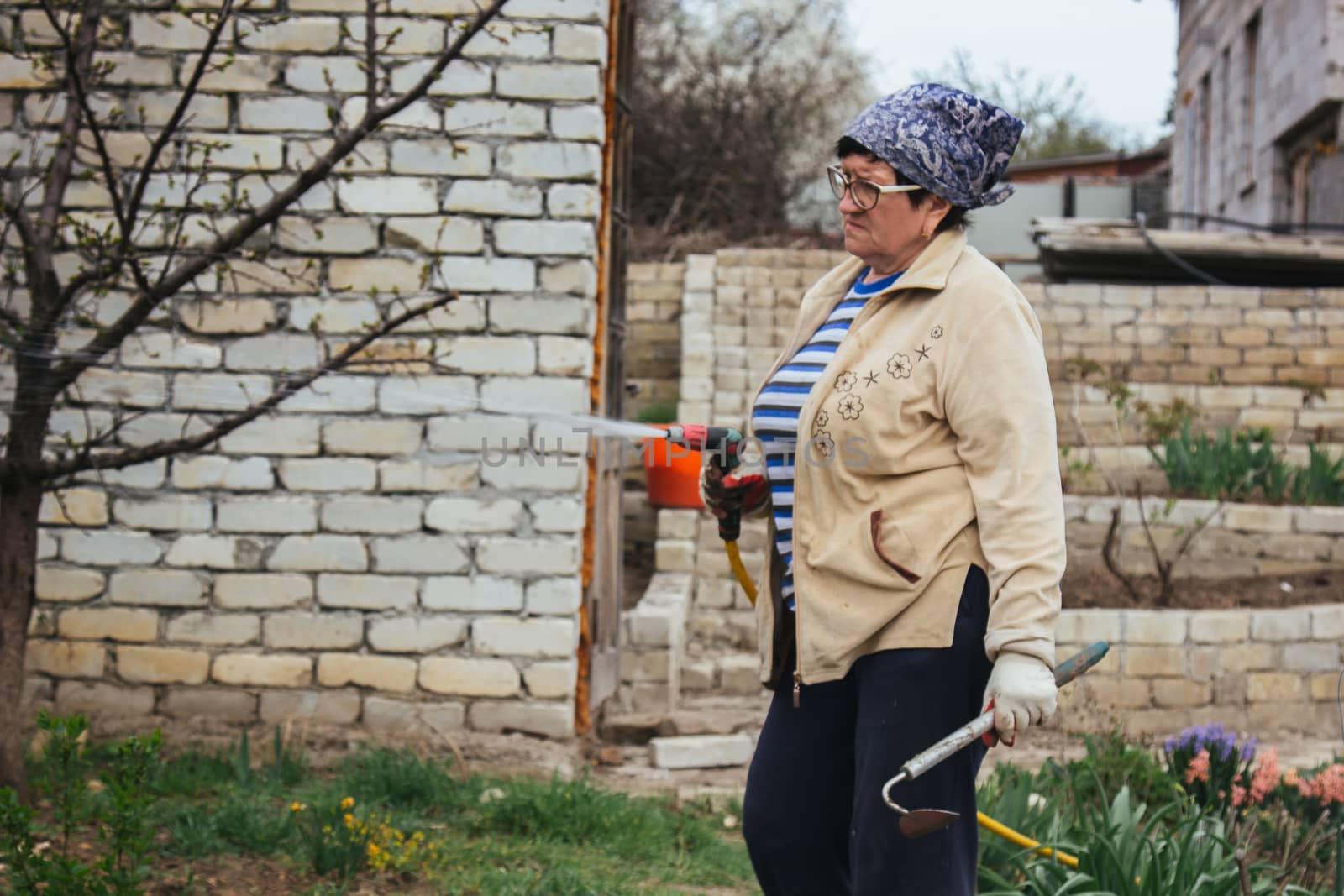 Woman holding garden water hose wearing colorful wellies watering garden by yulaphotographer