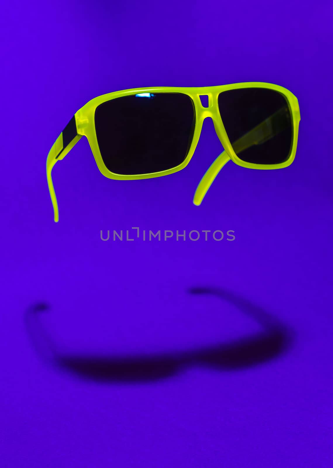 Bright green colour sun glasses in the air. Green floating in the air sunglasses on purple background. Lower shadow below the glasses. Minimalism summer concept.