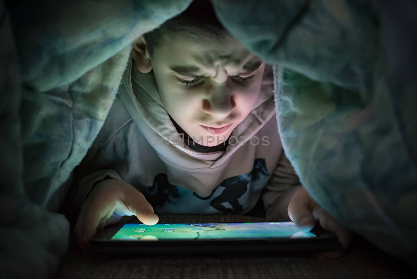 Child watching his tablet in the bed. Illuminated child face fro by deyan_georgiev