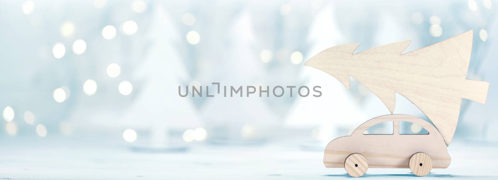 Wooden car carrying a christmas tree in front of dreamy and abstract glitter bokeh lights in forest background