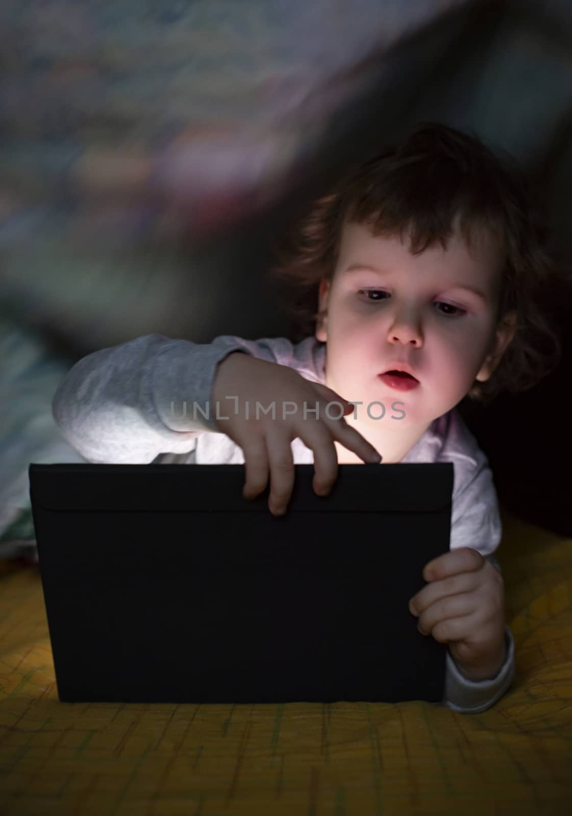 Little girl watching her tablet in the bed. Illuminated child fa by deyan_georgiev