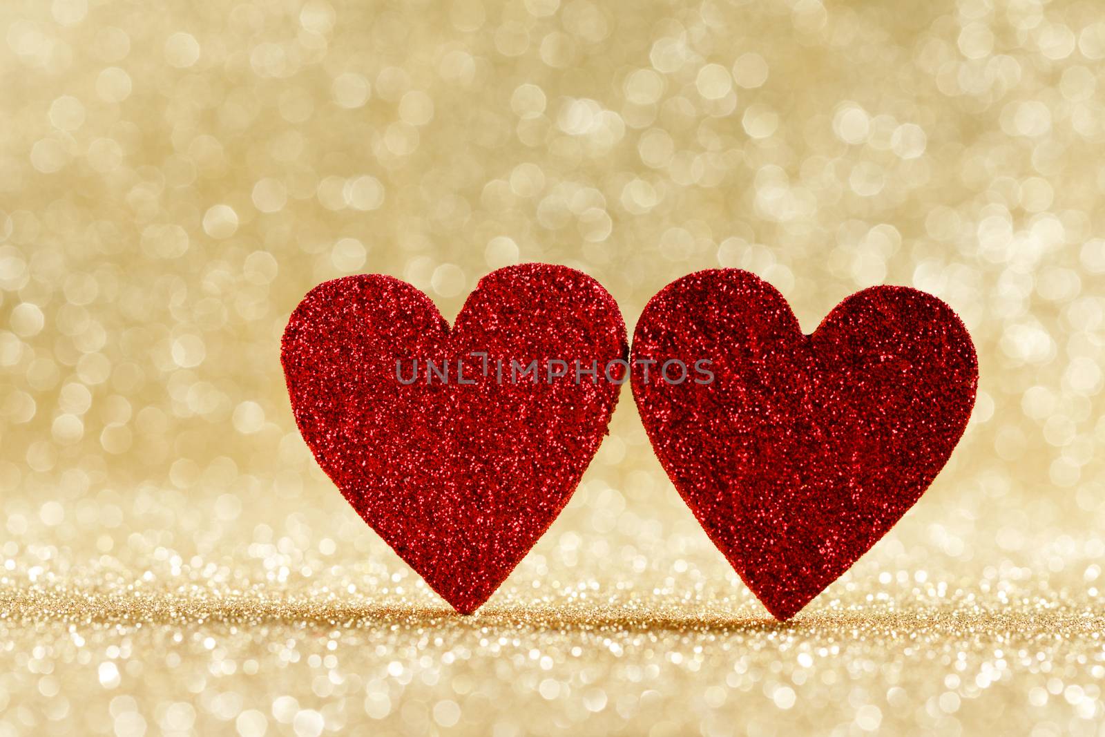 Two small handmade red glitter hearts on bright golden lights bokeh background Valentines day card