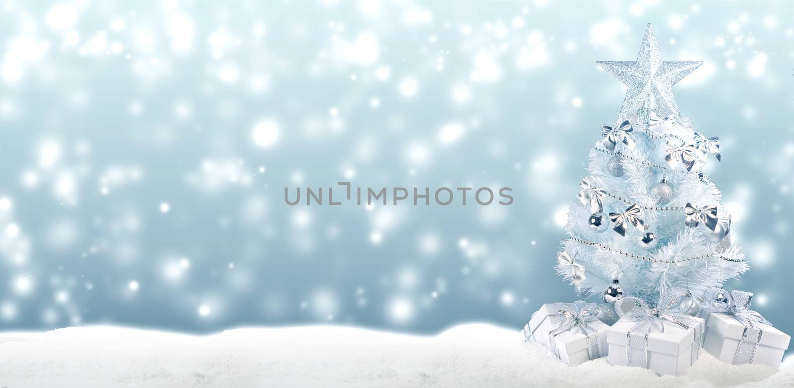 White christmas tree with silver decorations and gifts on snow on bokeh background