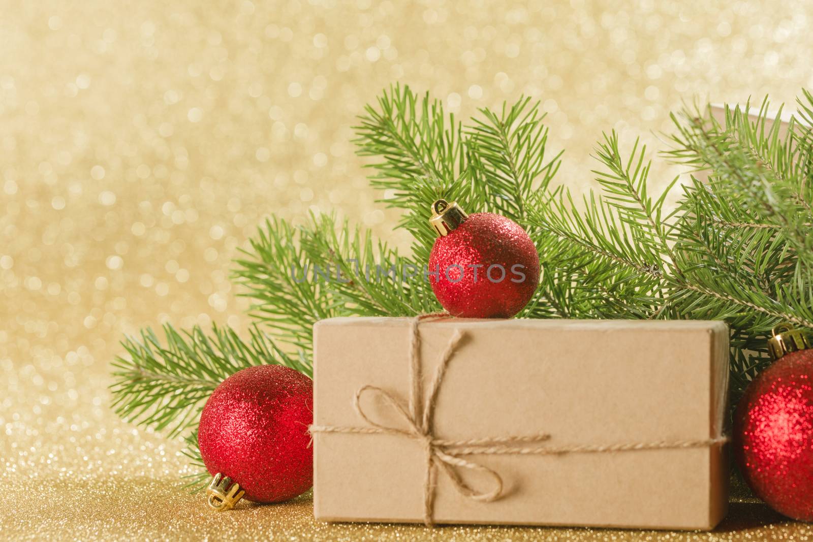 Christmas or new year decorations, craft paper gift box, fir tree branches on golden glitters background, copy space