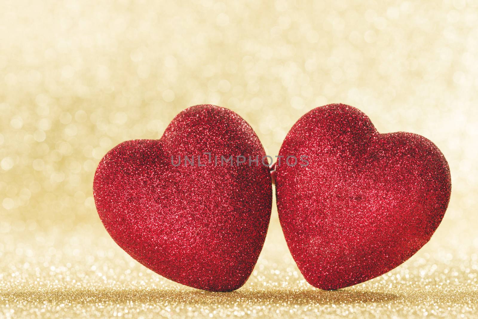 Two small handmade red glitter hearts on bright golden lights bokeh background Valentines day card