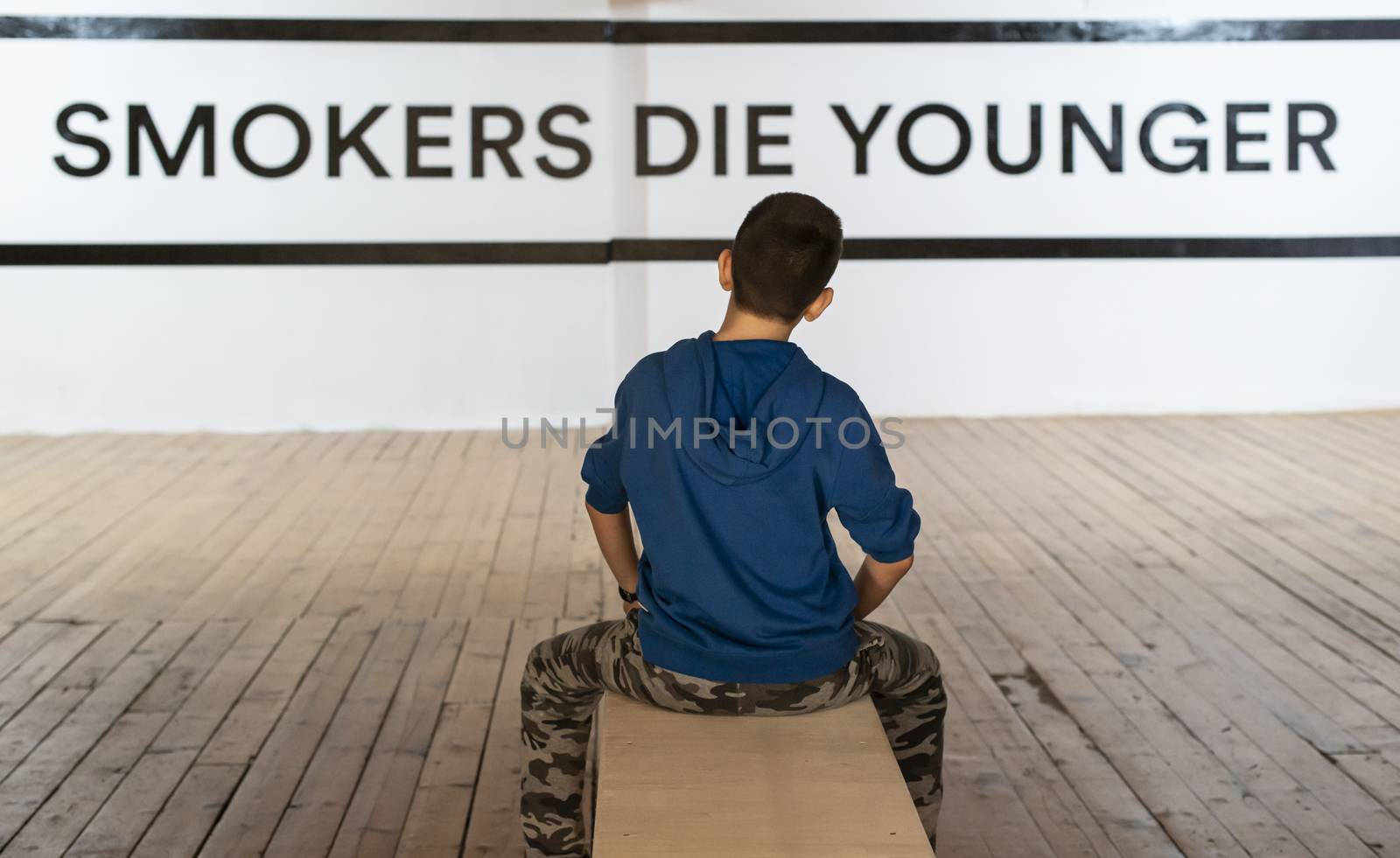 Teenager smoking and message on wall - Smokers die younger. No smoking concept with child. Casual clothes.