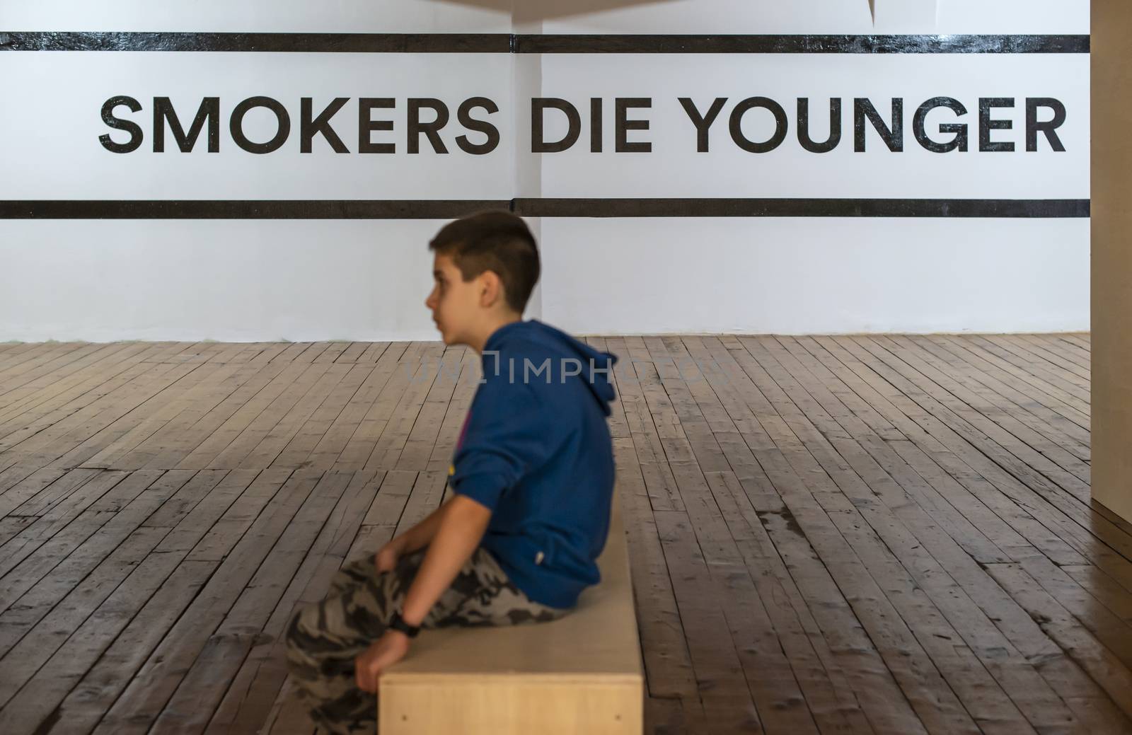 Teenager smoking and message on wall - Smokers die younger. No smoking concept with child. Casual clothes.