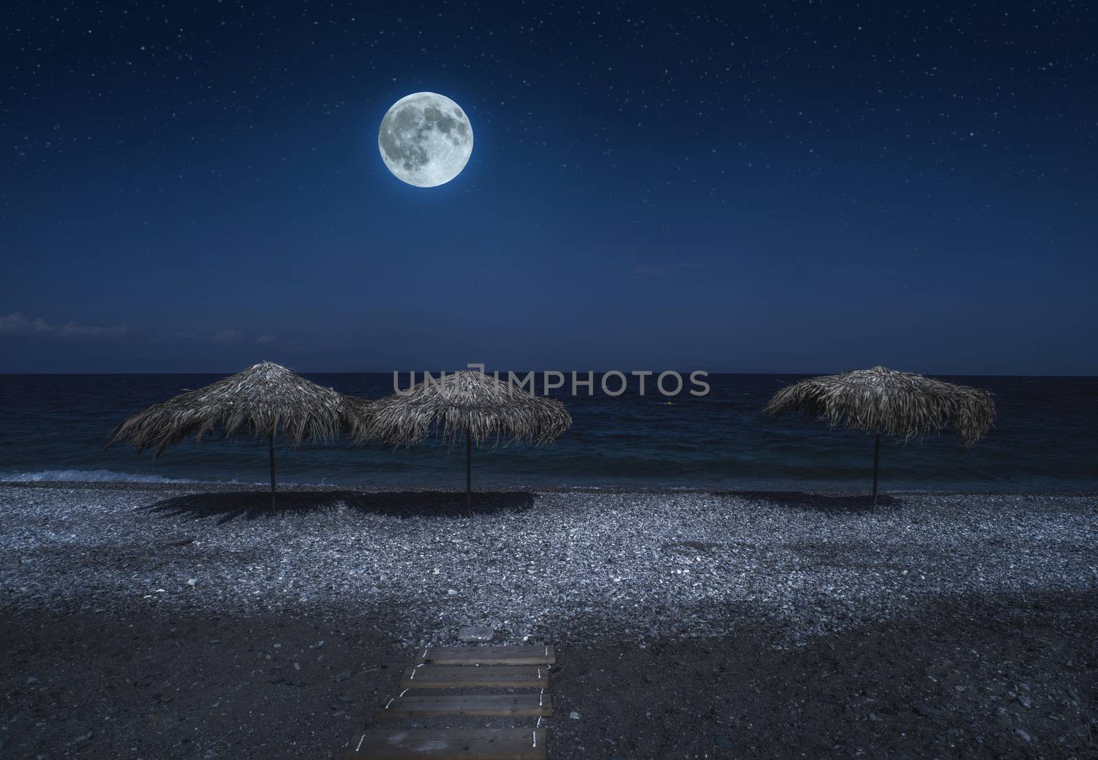 Straw umbrellas on the beach in the night. Moonlight on sea. Night starry sky. 