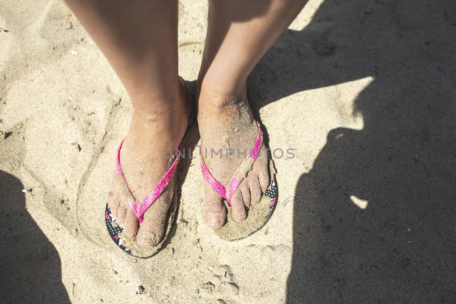 Woman feet with flip flops on the sand. Sunny day