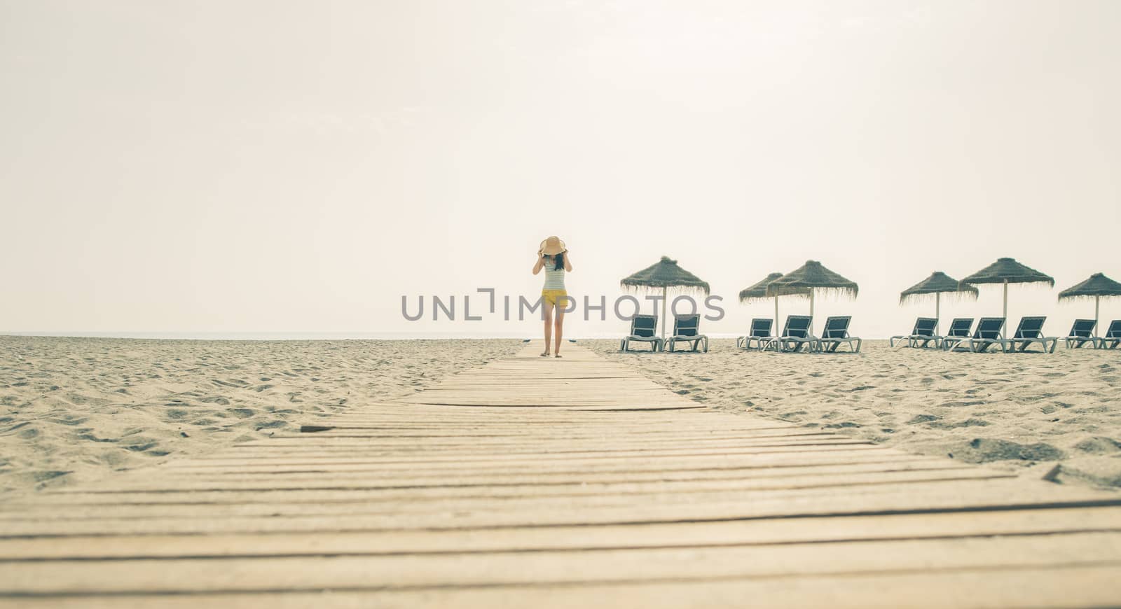 Woman with hat on wooden trail on the beach in the morning. Sunrise