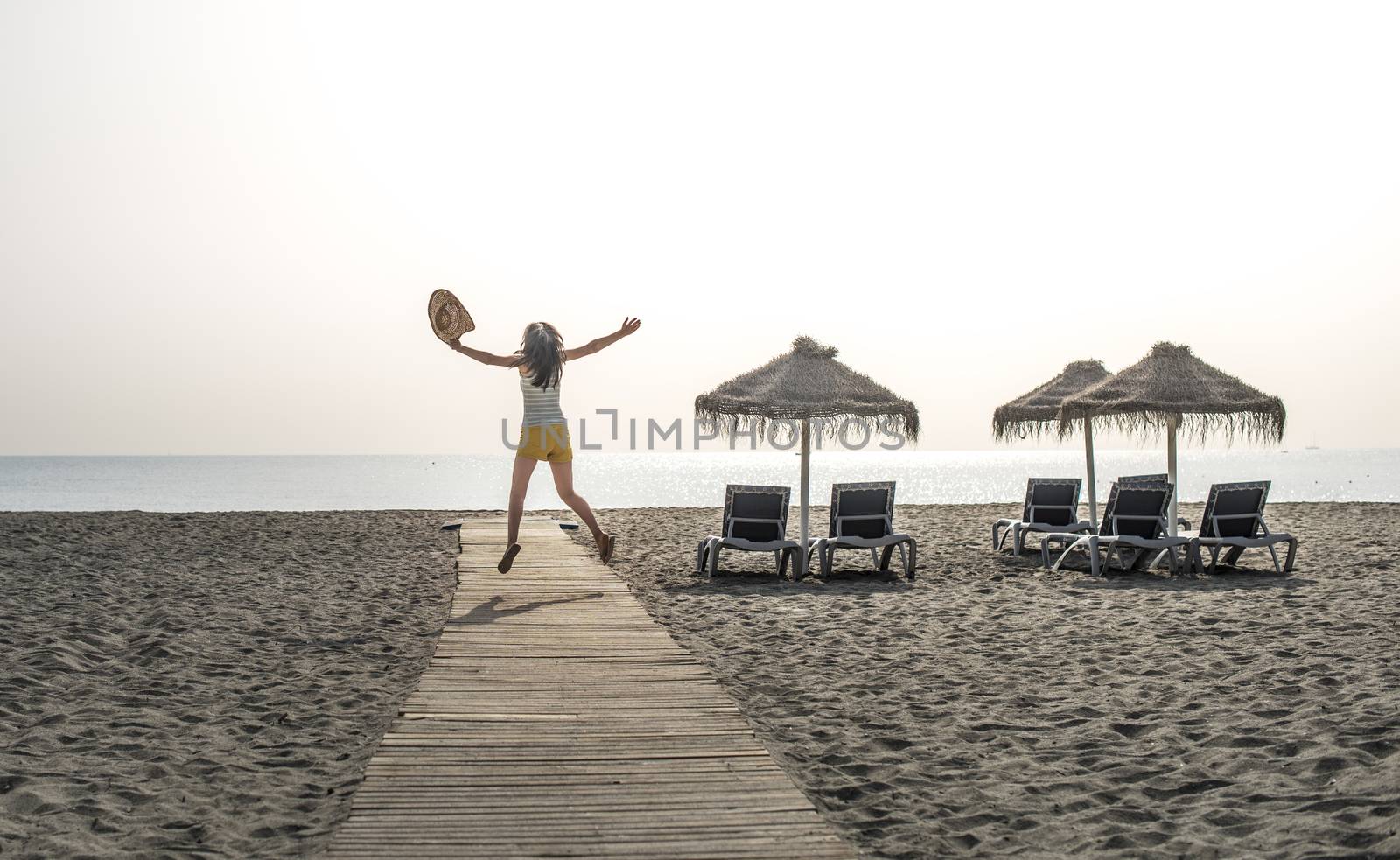 Wooden path to the beach, umbrellas and jumping woman