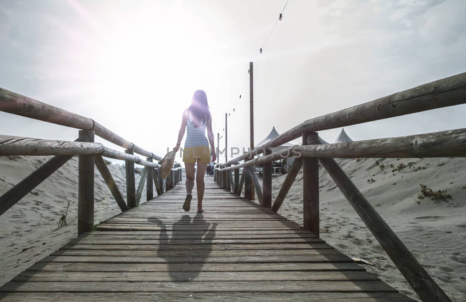 Woman with hat on wooden trail on the beach in the morning. Sunrise