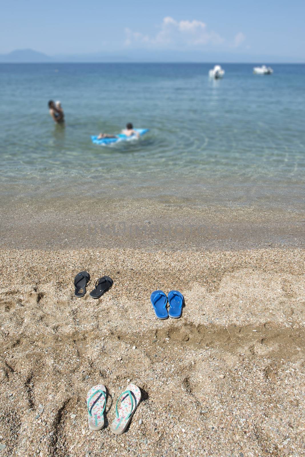 Slippers in the sand on the beach and people at sea. 