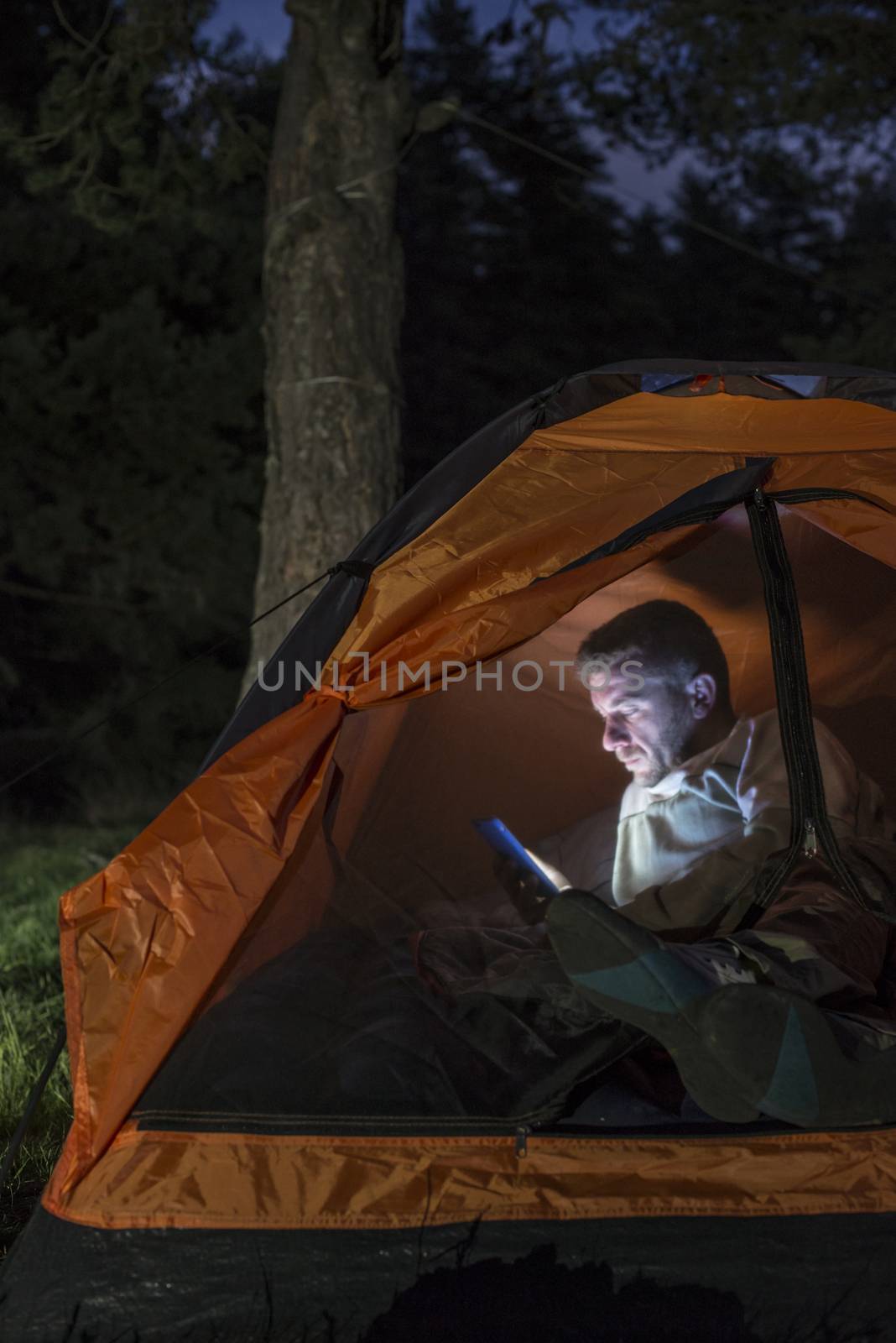 Man watching his smartphone in a tent. by deyan_georgiev