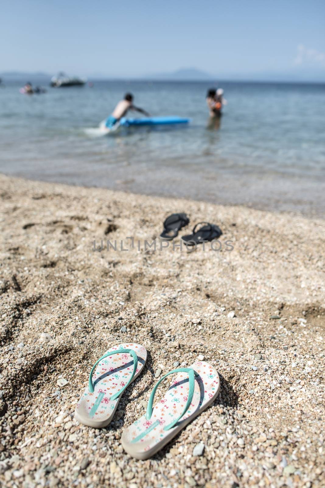 Slippers in the sand on the beach and people at sea. 