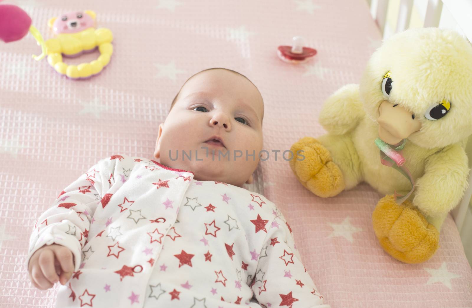 Baby girl in a bed with toys around by deyan_georgiev
