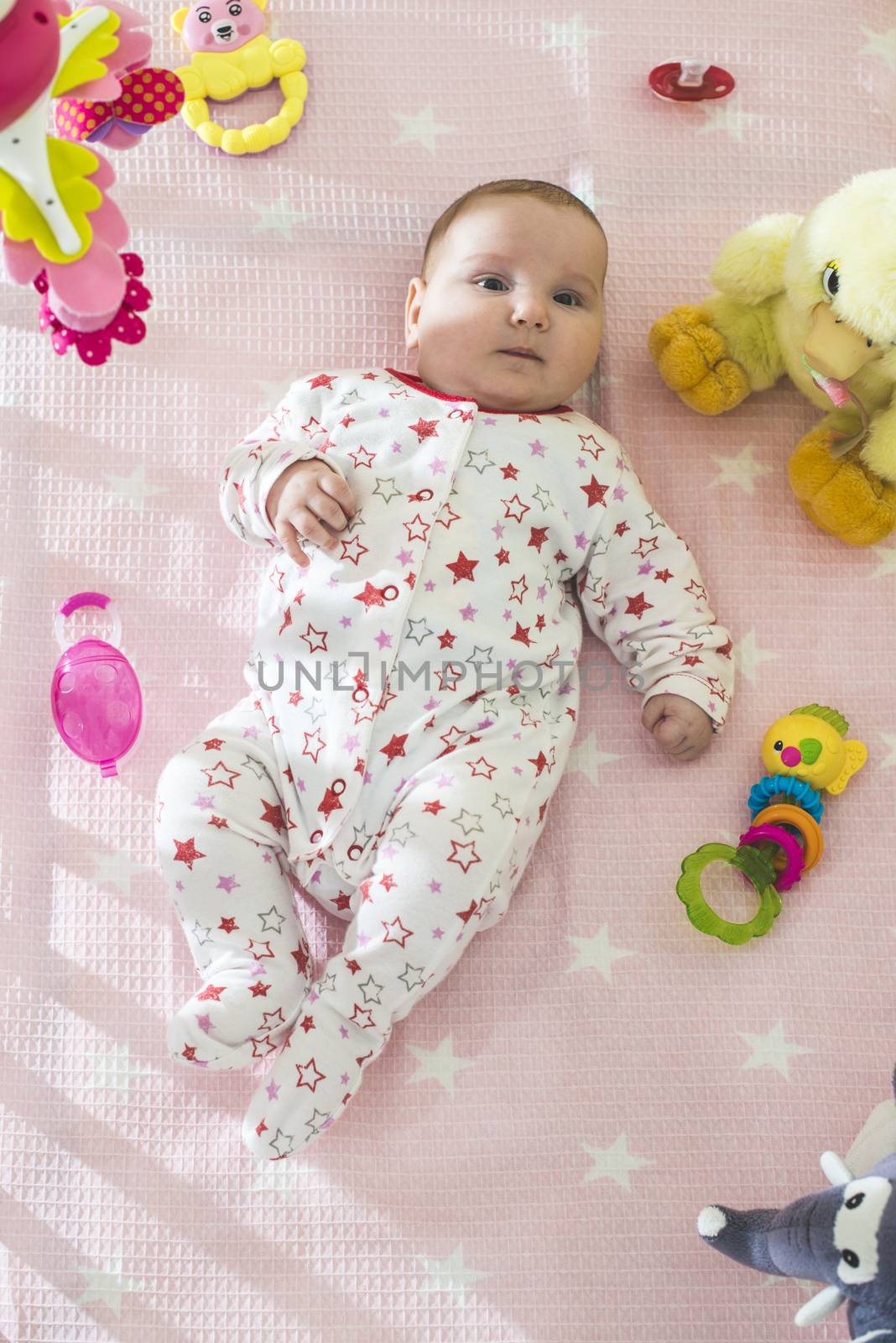 Baby girl in a bed with toys around. Pink tones