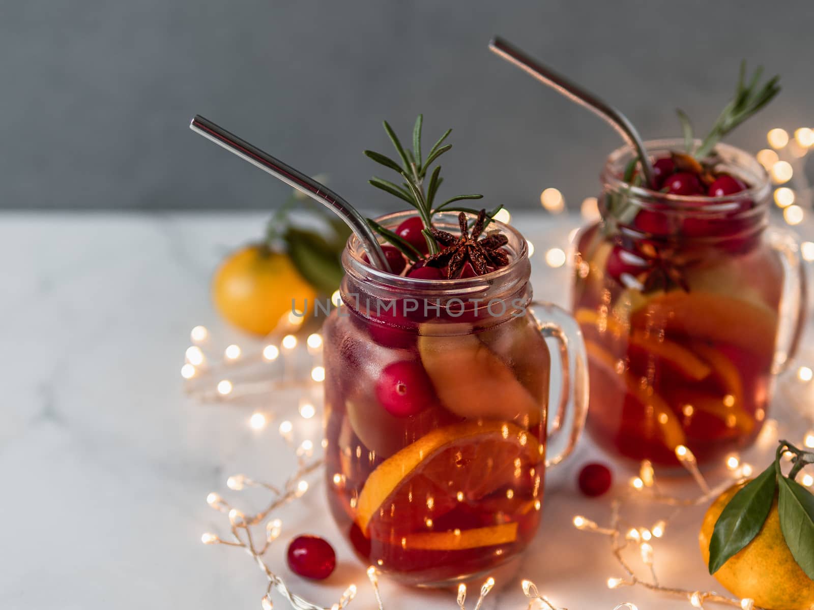 Winter sangria in mason jars with metal straws on christmas holiday background. Decorated fruit slice, cranberry and rosemary. Copy space for text or design. Horizontal. Decoration lighting chain