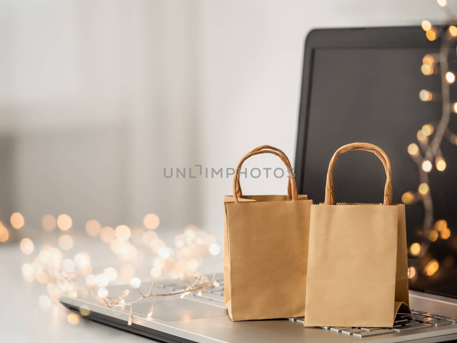 Winter holiday shopping online. Paper bags on notebook and decoration lighting chain. Copy space for text or design.