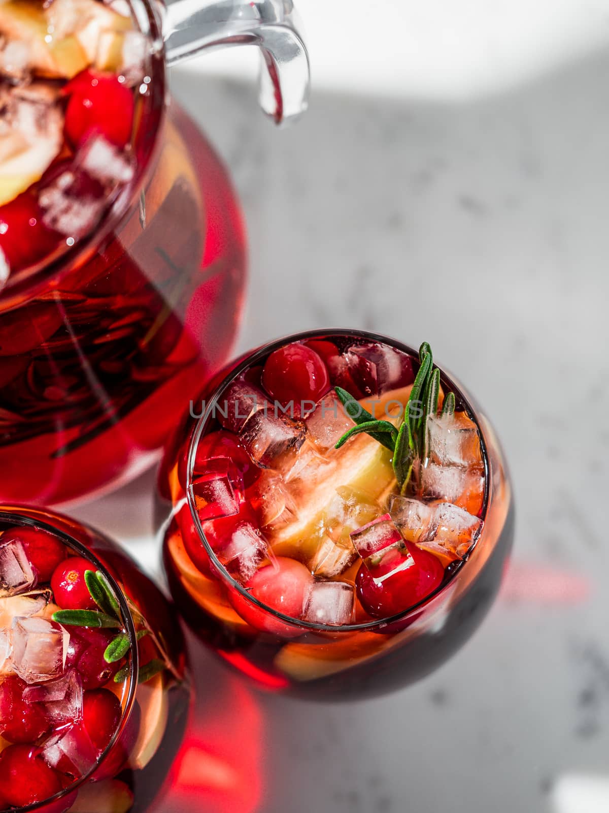 Winter sangria on tabletop with gray linen tablecloth. Glasses of sangria with fruit slice, cranberry and rosemary. Copy space for text or design. Top view or flat lay. Vertical.